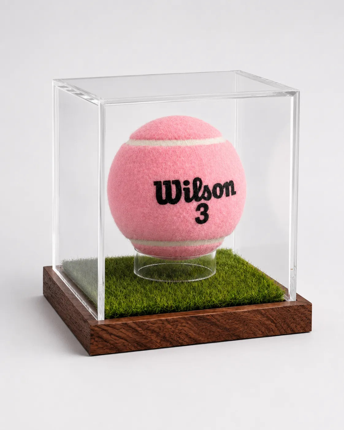 Angled view of a tennis ball display case with artificial grass and wooden base
