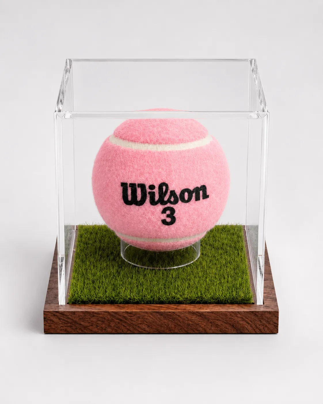 Angled view of a tennis ball display case with artificial grass and wooden base